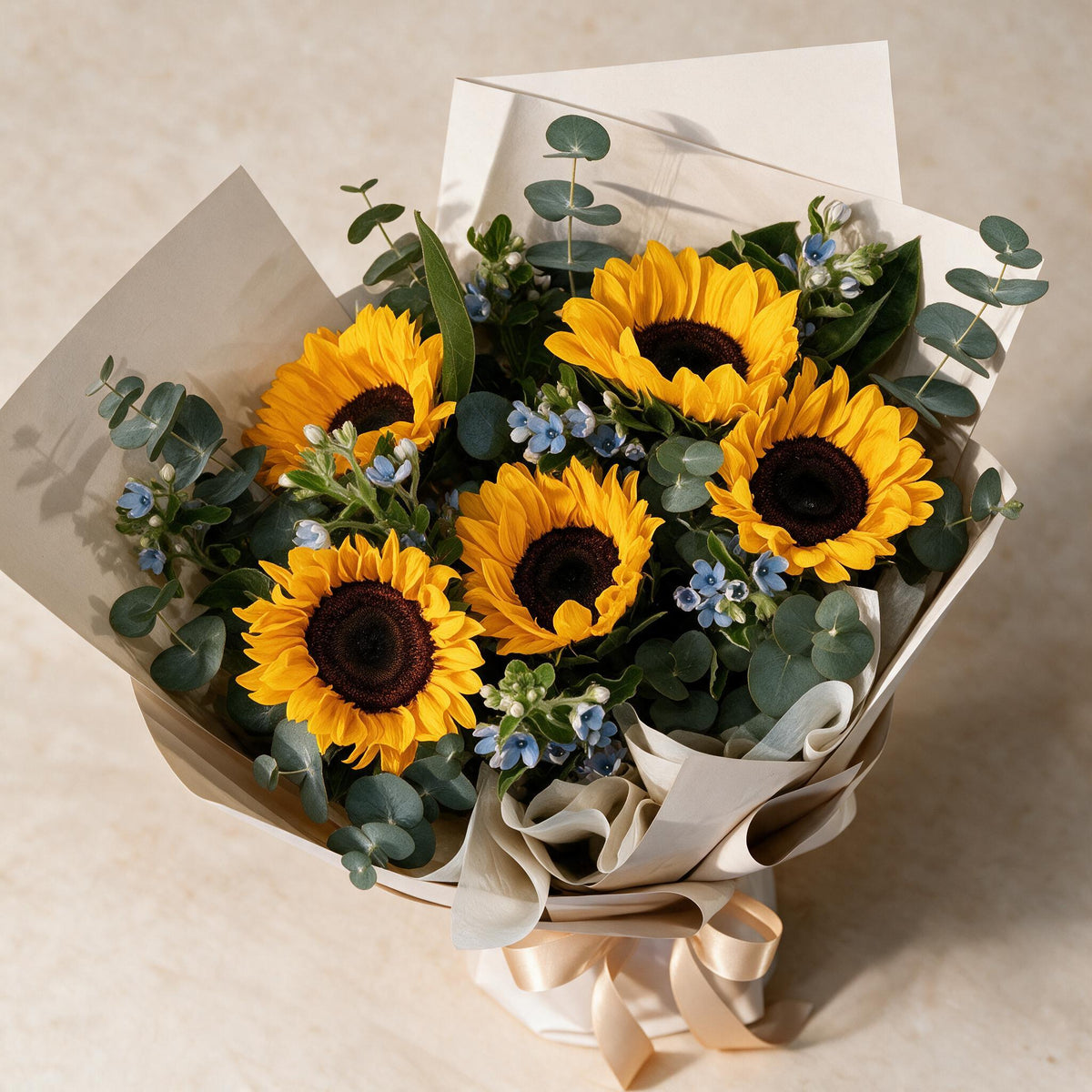 Top view of the Sunny fresh flower bouquet of five sunflowers with blue oxypetalum and eucalyptus
