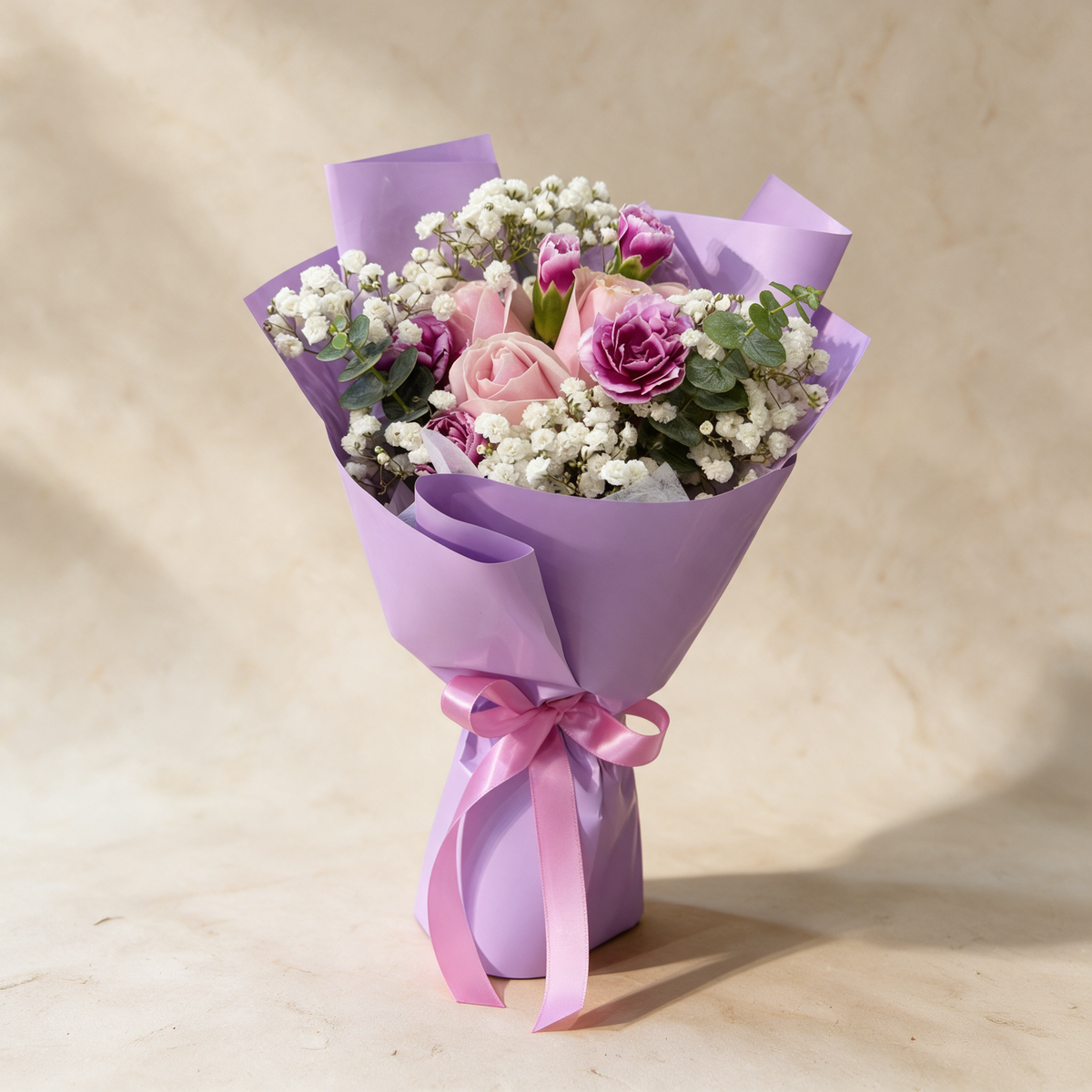 Whisper fresh flower bouquet of three pink roses with spray carnations, baby’s breath and eucalyptus in lilac wrap