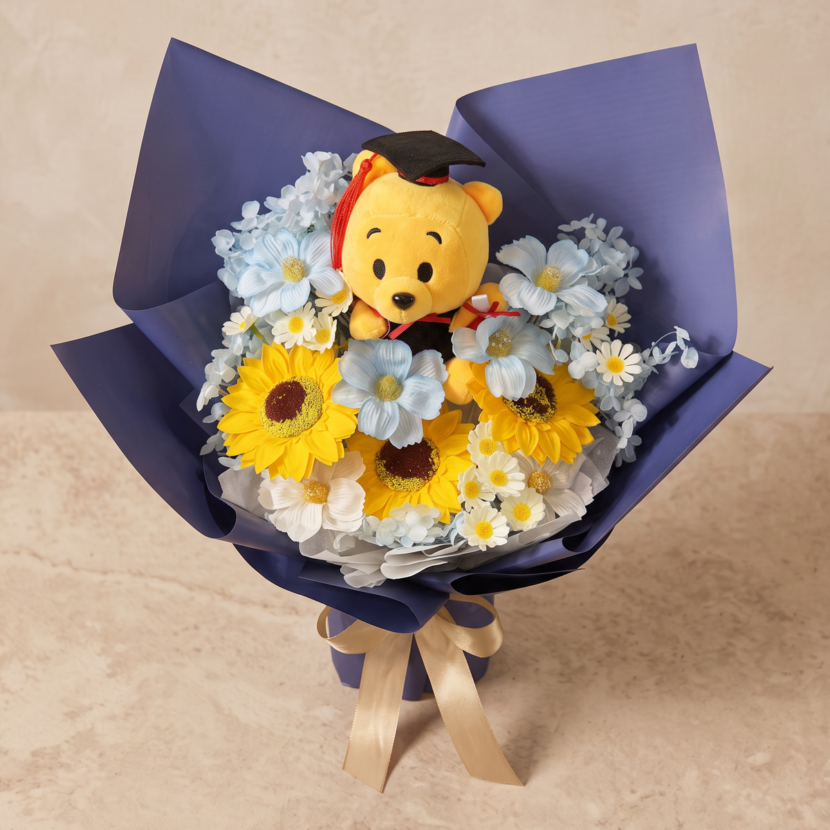 Top view of the Honours soap flower bouquet of sunflowers, blue cosmos and chamomile with a Convo Bear in cap